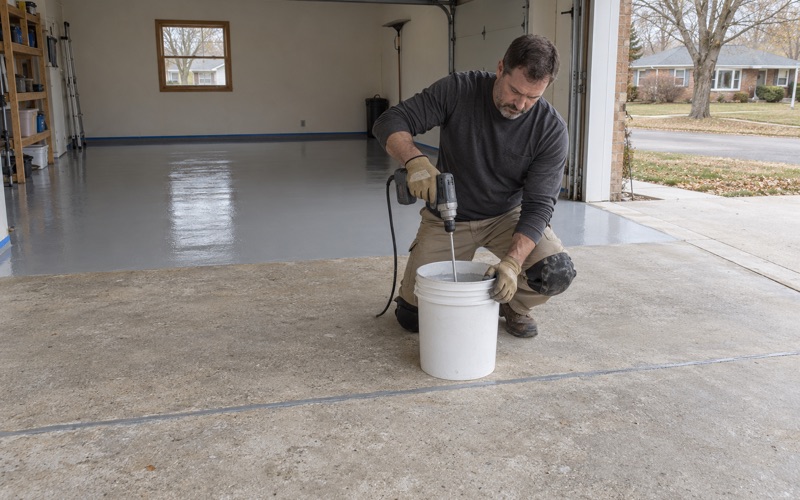 Two-part epoxy base coat mixed in a Janesville ranch garage, the back half of the ground slab already coated.